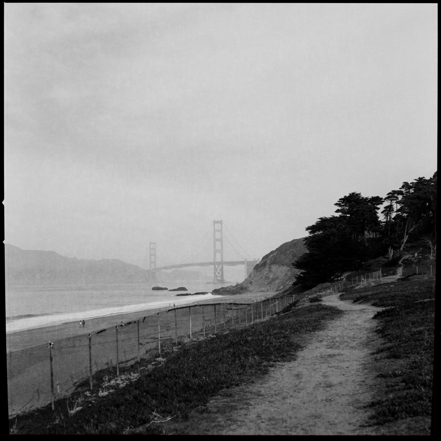 A path along a fence along Baker Beach with the Golden Gate Bridge in the background