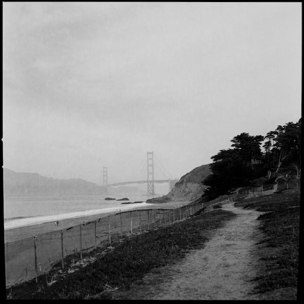 A path along a fence along Baker Beach with the Golden Gate Bridge in the background